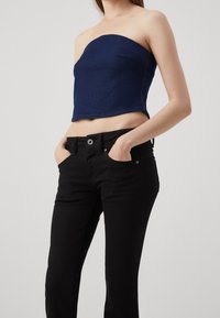 Haut sans manches en denim bleu foncé avec une coupe ajustée, associé à un jean noir comportant une poche avant et un détail de bouton en métal.