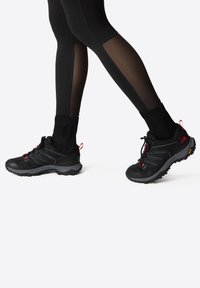 Czarne buty sportowe z teksturowaną cholewką, z czerwonymi akcentami, bezpiecznym systemem sznurowania oraz wytrzymałą podeszwą zaprojektowaną z myślą o przyczepności.