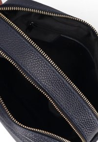 Interno di una borsa in pelle blu scuro con chiusure a zip dorate a contrasto. Presenta un esterno texturizzato e una fodera nera liscia, con scomparti in evidenza.