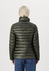 Grønn, pufferjakke med horisontalt quiltet design, høy krage og glatt tekstur; kombinert med blåjeans. Ingen synlig merkevare.