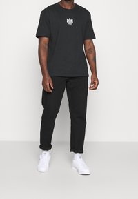 Svart bomullströja med vit logga, kombinerad med svarta byxor och vita sneakers. Fokusera på en avslappnad och ledig passform.