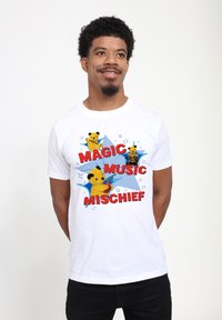 Bílé bavlněné tričko s barevným grafikou tří žlutých medvídků a textem "MAGIC MUSIC MISCHIEF" tučnými červenými písmeny.