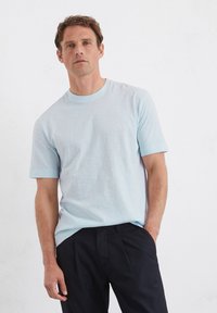Lichtblauw kortemouwen t-shirt van een zachte, gladde stof met een ronde halslijn en subtiele textuur, gecombineerd met donkere broeken.