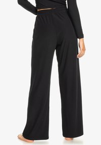 Black wide-leg pants in ribbed fabric, featuring an elastic waistband for comfort. The texture is smooth with a slight sheen.