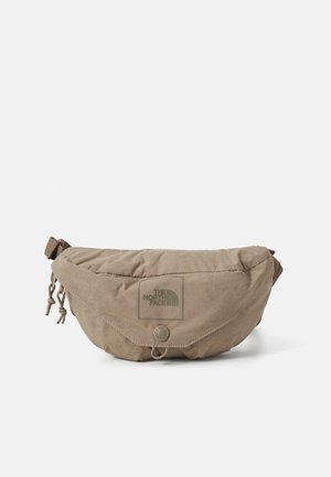 Beige North Face waist bag with zipper, adjustable strap, front flap, logo, and pull tab on a white background.