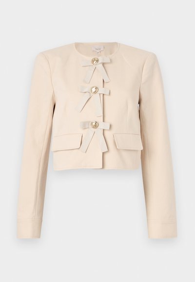 Cropped beige jacket with long sleeves, featuring four fabric bows and large gold buttons, complemented by two front pockets. Smooth texture.