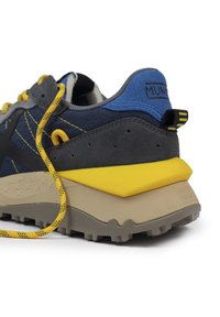 Zapatilla gris y azul con acentos amarillos, parte superior de gamuza y tela texturizadas, gruesa mediasuela beige y suela exterior de goma negra con tracción.