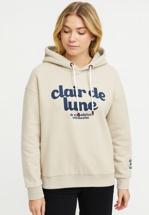 Beige hoodie with navy graphic text, drawstrings, and ribbed cuffs. Soft texture, loose fit, and printed details on the sleeves.