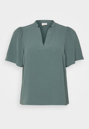 Türkiisi bluus peene tekstuuriga kangast, V-dekolteega ja lühikeste puffvarrukatega. Lõdva fitiga sirge lõikega, ilma nähtavate kaunistusteta.