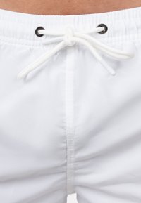 Costumi da bagno bianchi con vita elastica e cordoncino, occhielli neri e una texture di tessuto liscia e leggera.