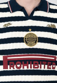 Chemise à col rayée bleu marine et blanc avec le texte « PROHIBITED », un emblème de globe et « Berlin, Allemagne » sur le devant.