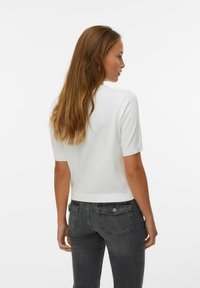 Top bianco a maniche corte con collo rotondo e rifiniture a costine, abbinato a jeans grigio scuro con taglio classico e tasche posteriori.