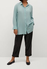 Chemise bleu clair à manches longues avec boutons, coupe décontractée, associée à un pantalon noir à jambes larges et des ballerines noires. Tissu lisse, look casual.