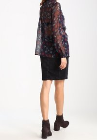 Blusa trasparente blu navy con stampa floreale, abbinata a una gonna di jeans nera. L'outfit presenta maniche lunghe e stivaletti marroni fino alla caviglia.