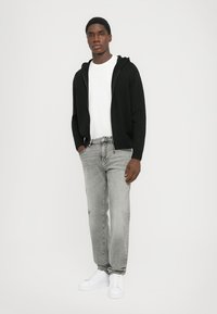 Sort zip-up hættetrøje, hvid t-shirt, grå jeans, hvide sneakers. Afslappet outfit med løs pasform og enkel design. Ingen bemærkelsesværdige mønstre.