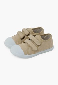 Chaussures en toile beige avec deux sangles réglables en Velcro et un capuchon de orteil en caoutchouc gris. Semelle plate et texturée offrant une bonne adhérence.