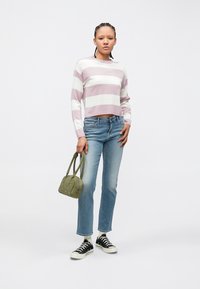 Pull rayé rose et blanc raccourci à manches longues, associé à un jean bleu clair à jambes droites et des baskets noires ; tenant un sac vert.