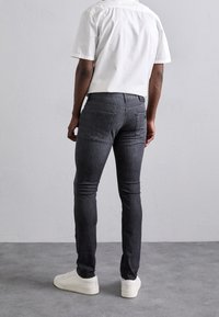 Mörkgrå slim-fit jeans med en slät yta, med bakfickor och medelhög midja, kombinerat med vita sneakers och en kortärmad vit skjorta.