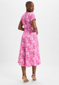 Floral mid-length dress in pink and white tones, short sleeves, fitted waist, flared skirt with pleats, paired with nude high-heeled sandals.