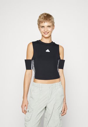 Top sportivo nero corto con aperture sulle spalle, con logo bianco, colletto a coste e dettagli a strisce sui lati. Abbinato a pantaloni cargo chiari.