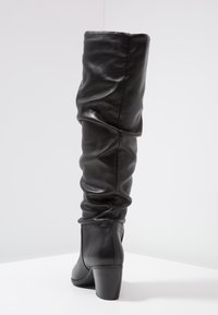 Bottes en cuir noir, montant jusqu'au genou, avec un design froncé, dotées d'un talon épais et d'une texture lisse. Pas de motifs ni de détails métalliques visibles.