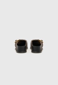 Black and brown slip-on shoes with a smooth texture, gold hardware accents, and a structured sole. Minimalist design with open back.