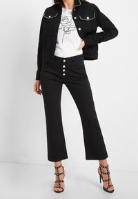 Black denim jacket with studded details, white t-shirt featuring rose graphic, black flared jeans with button fly, and strappy black high heels.