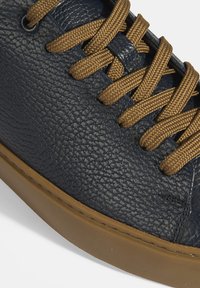 Marineblaue Ledersneaker mit strukturierter Oberfläche, braunen Schnürsenkeln und einer Gummisohle. Verfügt über eine Naht entlang der Kante und Ösen für die Schnürsenkel.