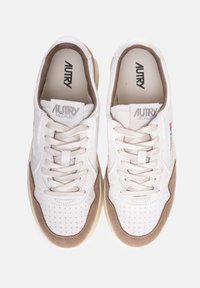 Zapatillas de cuero blanco con detalles en ante beige, puntera perforada, cordones planos y logo en relieve en la lengüeta. Suela de goma redondeada.