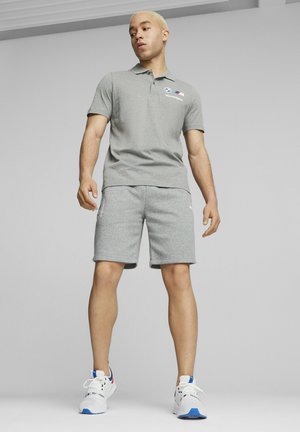 Szara koszulka polo z logo, dopasowane szare szorty i białe trampki z niebieskimi akcentami. Casualowy sporty strój pokazany na modelu.