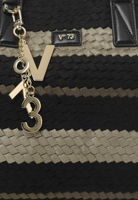 Bolso texturizado con un patrón de rayas en negro y beige, con acentos de hardware dorado y un charm que muestra "V", "O" y "3" en letras gruesas.