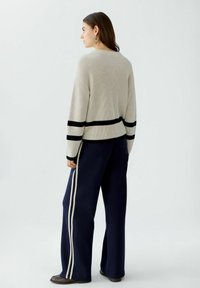 Hellbeige gerippter Pullover mit schwarzen Streifen am Saum und an den Ärmelbündchen, kombiniert mit marineblauen, weit geschnittenen Hosen mit elfenbeinfarbenen Seitenstreifen.