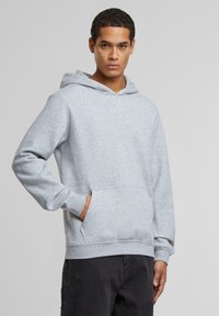 Grå hettegenser laget av mykt stoff, med en kengurulomme, ribbede mansjetter og en avslappet passform.