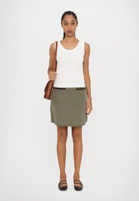Hvit ribbet tanktop, olivengrønn, kviltet miniskjørt med to lommer og svarte detaljer, sammen med en brun skulderveske og flate sko.