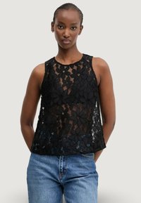 Top in pizzo nero con design floreale, tessuto trasparente, scollatura rotonda e senza maniche, abbinato a jeans blu casual.