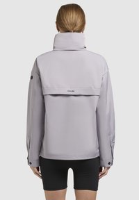 Light purple jacket with a high collar, boxy design, buttoned cuffs, and a rear flap detail. Made of smooth, lightweight material.