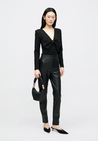 Black long-sleeve bodysuit with a large bow detail at the chest, paired with sleek black faux leather pants and a small handbag.