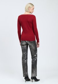 Rode longsleeve trui met een afgeronde achterhalslijn, gecombineerd met glanzende metallic grijze rechte broek en zwarte stilettodames.