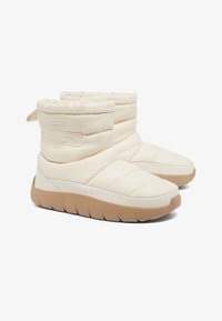 Botas de tobillo acolchadas de color crema con una textura suave, que cuentan con una parte superior acolchada, suela de goma texturizada y una lengüeta en la parte trasera para facilitar su uso.