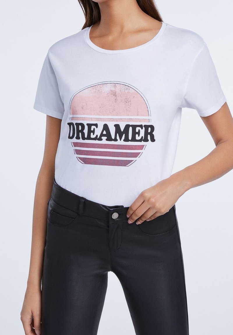 T-shirt blanc en coton avec un graphisme circulaire contenant le mot « DREAMER » en police noire gras et des rayures aux tons pastel variés.