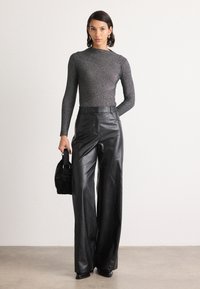 Pantalons larges en cuir noir avec une texture lisse, associés à un haut ajusté en côtes de couleur sombre avec des rayures diagonales aux reflets métalliques.