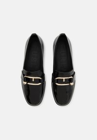 Black leather loafers with a glossy finish, featuring a gold buckle accent across the front and a rounded toe design.