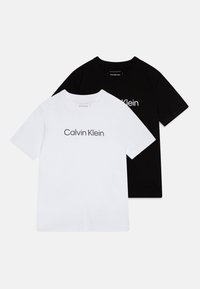 Pack of two t-shirts: one white and one black, both made of cotton with short sleeves and a round neck. Each features "Calvin Klein" in front.