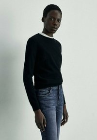 Černý svetr s kulatým výstřihem, nošený přes modré džíny. Svetr má měkkou texturu a džíny mají klasický střih.
