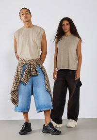 Khaki ermeløse skjorter, brede denimshorts, rutete skjortebundtet i livet, svarte baggy bukser og forskjellige sneakersstiler.