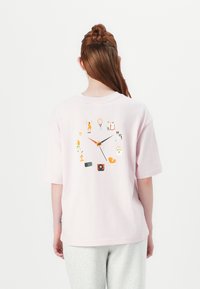 Light pink cotton t-shirt with short sleeves, featuring a colorful clock design on the back, incorporating various playful icons.