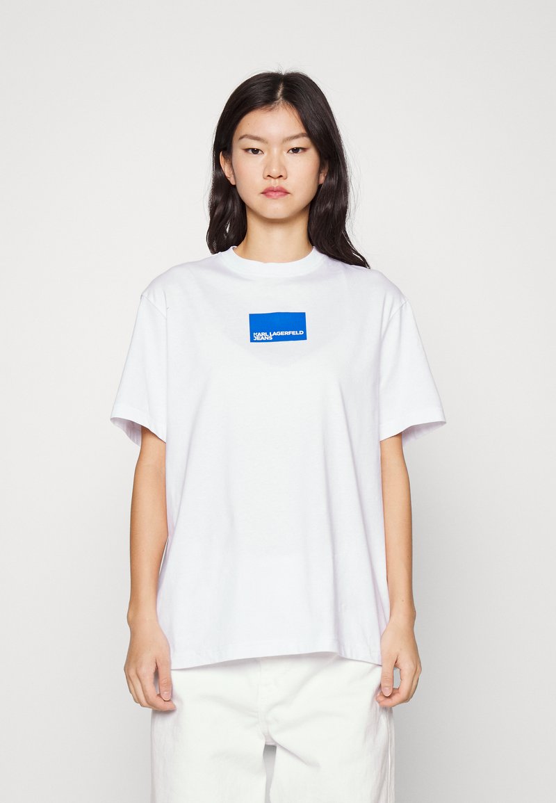 Hvid bomulds T-shirt med korte ærmer, der har et blåt rektangulært logo på brystet. Rund halsudskæring, afslappet pasform, glat tekstur.