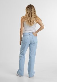 Lyseblå høy midje jeans med avslappet passform og rette ben. Denim materiale med en bleket finish og to baklommer.