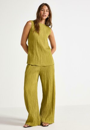 Dvoudílný outfit z texturované, mechově zelené látky. Vrchní část je bez rukávů s volnějším střihem; kalhoty jsou široké a splývavé.