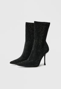 Μαύρες γόβες αστραγάλου με λαμπερή, υφαντή επιφάνεια. Μυτερή μύτη και ψηλός στιλέτο τακούνι. Εφαρμοστή σχεδίαση που αγκαλιάζει τον αστράγαλο.